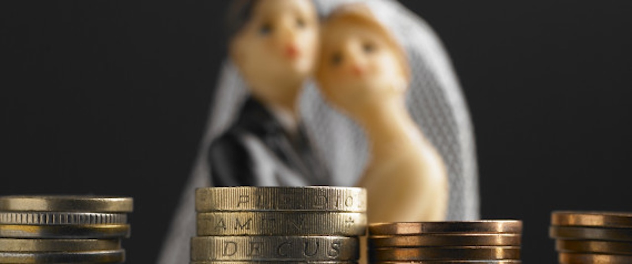 Bride and groom wedding figure standing in front of a stack of coins (Concept of the cost of weddings/pre nutual agreement)